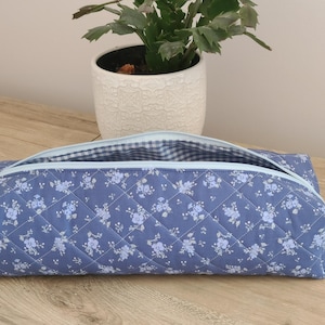 A blue quilted pencil case with a floral pattern sits on a wooden surface, with a potted plant in the background.