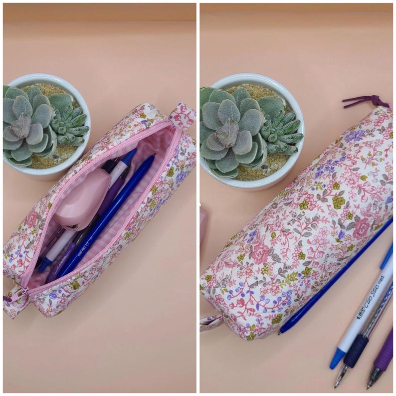 Puede incluir: Un estuche cil&iacute;ndrico de tela con un estampado floral en tonos rosa, verde y morado. El estuche se muestra abierto, revelando un interior rosa con bol&iacute;grafos y una grapadora, y cerrado, con tres bol&iacute;grafos colocados al lado.