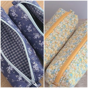 Puede incluir: Dos estuches acolchados. El estuche de la izquierda es azul con un patr&oacute;n floral blanco, una cremallera azul claro y un interior de cuadros vichy azul y blanco. El estuche de la derecha tiene un estampado floral amarillo y azul.