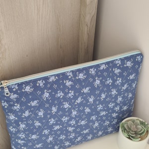 May include: A blue quilted laptop sleeve with a white floral pattern and a light blue zipper. The sleeve is lying on a white surface.