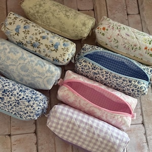 Puede incluir: Una colecci&oacute;n de ocho estuches rectangulares con cremallera que presentan varios patrones de tela floral y de cuadros vichy. Los estuches est&aacute;n acolchados e incluyen dise&ntilde;os en azul, blanco, rosa y lavanda, con algunos forros interiores a juego.
