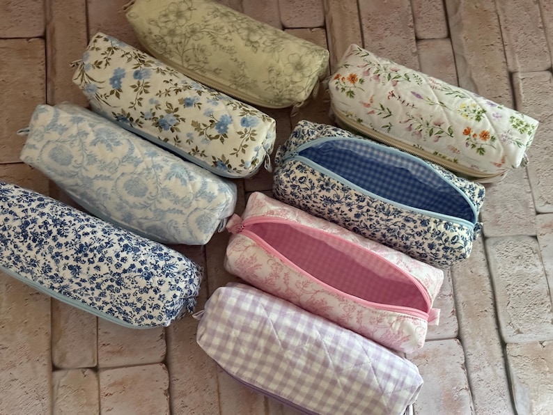 Puede incluir: Una colecci&oacute;n de ocho estuches rectangulares con cremallera que presentan varios patrones de tela floral y de cuadros vichy. Los estuches est&aacute;n acolchados e incluyen dise&ntilde;os en azul, blanco, rosa y lavanda, con algunos forros interiores a juego.