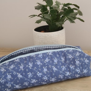 A blue quilted bag with a floral pattern sits on a wooden surface, with a potted plant in the background.