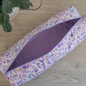 A floral patterned pencil case with a purple lining is placed on a wooden surface next to a potted plant.