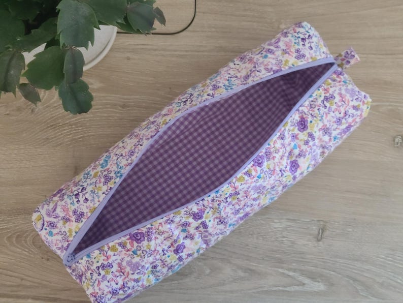 A floral patterned pencil case with a purple lining is placed on a wooden surface next to a potted plant.