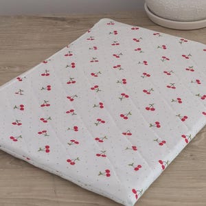 A white quilted mat with a repeating pattern of red cherries on a wooden surface.