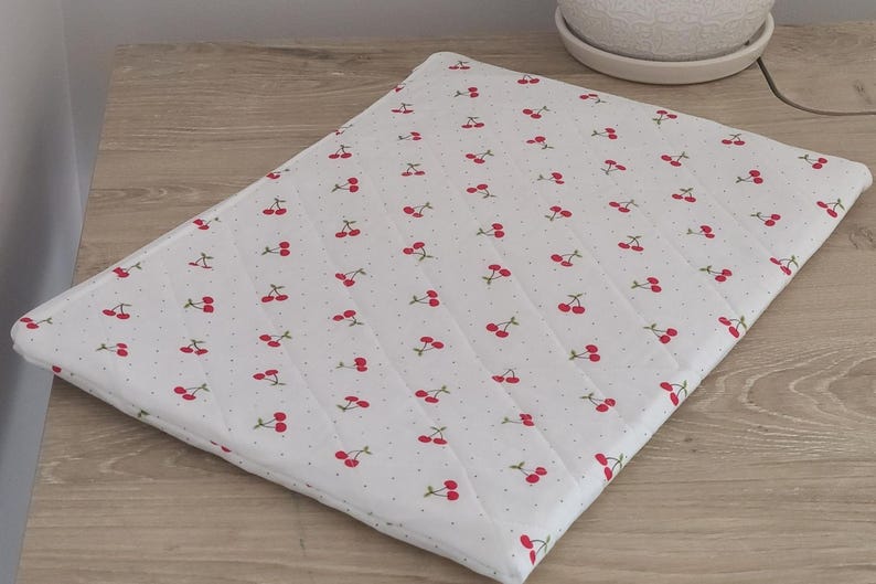 A white quilted mat with a repeating pattern of red cherries on a wooden surface.