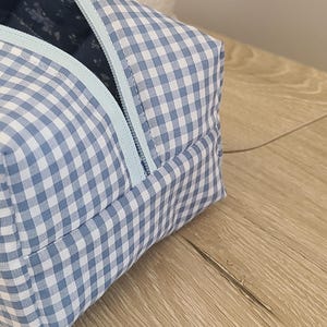 A blue and white checkered bag with a zipper closure is placed on a wooden surface.