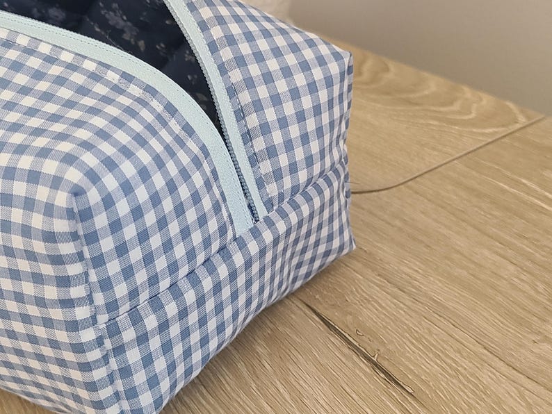 A blue and white checkered bag with a zipper closure is placed on a wooden surface.