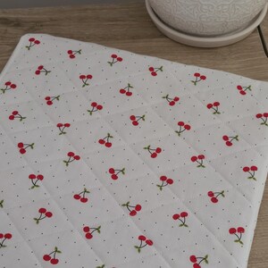 a white quilted mat with a repeating pattern of red cherries on a wooden surface.