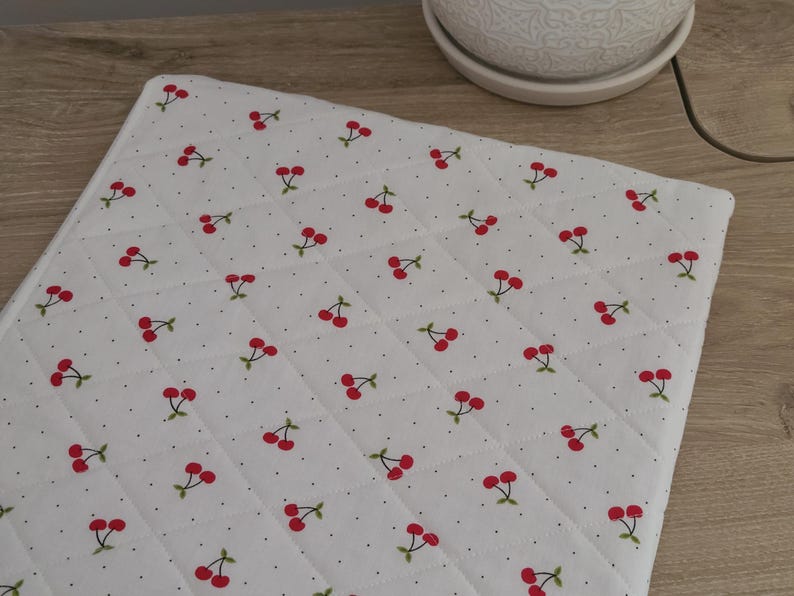 a white quilted mat with a repeating pattern of red cherries on a wooden surface.