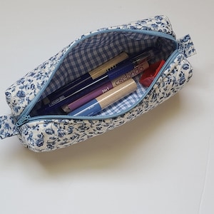 A blue and white floral pencil case containing various writing instruments is shown on a white surface.
