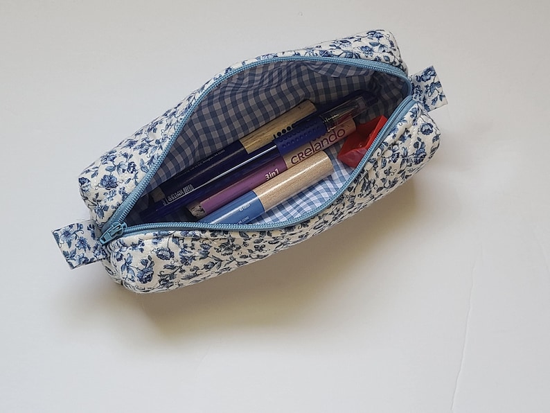 A blue and white floral pencil case containing various writing instruments is shown on a white surface.