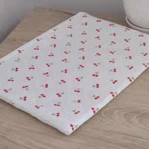 A white cloth with a repeating pattern of red cherries is placed on a wooden surface.
