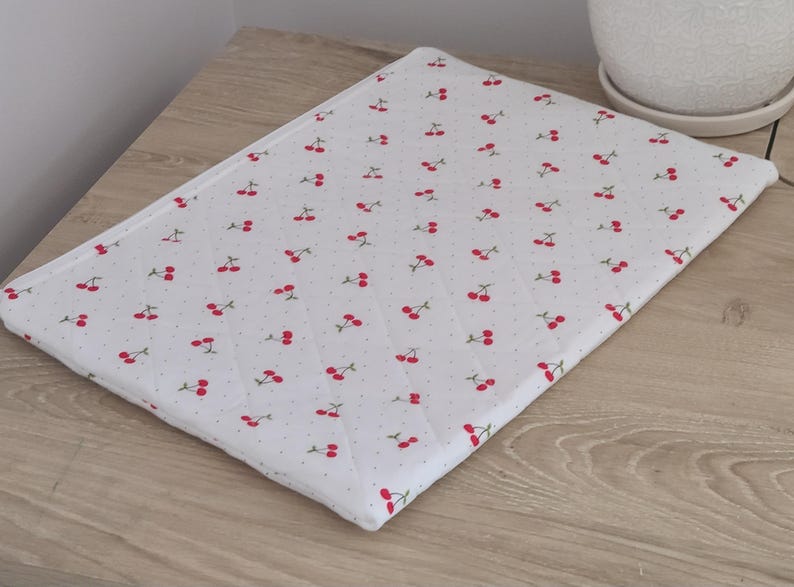 A white cloth with a repeating pattern of red cherries is placed on a wooden surface.