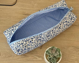 Peut inclure: Une trousse rectangulaire en tissu avec un motif floral bleu et blanc à l'extérieur et une doublure à carreaux vichy bleu clair et blanc. La trousse est dotée d'une fermeture éclair bleu clair sur le dessus et d'une structure souple.