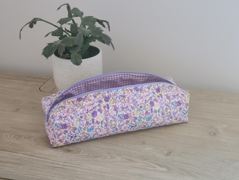 A floral patterned pencil case sits on a wooden surface next to a potted plant.