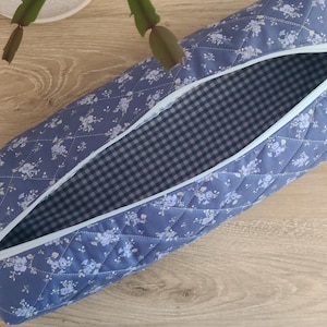 A blue and white quilted bag with a checkered lining is open and placed on a wooden surface.