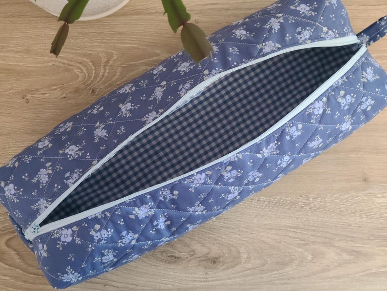 A blue and white quilted bag with a checkered lining is open and placed on a wooden surface.
