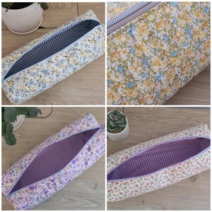 May include: A rectangular fabric pencil case featuring a floral pattern in shades of yellow, blue, and purple on a white background. The interior is lined with a blue and white or purple and white gingham check fabric and has a zipper closure.