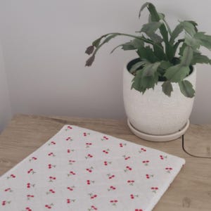 A potted plant with green leaves sits on a wooden surface, accompanied by a white cloth with red cherries on it.