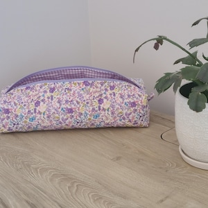 A floral patterned pencil case sits on a wooden surface next to a potted plant.