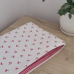 a white quilted bag with a red and white checkered lining, placed on a wooden surface next to a potted plant.