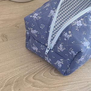 A blue and white floral patterned bag with a zipper closure is placed on a wooden surface.