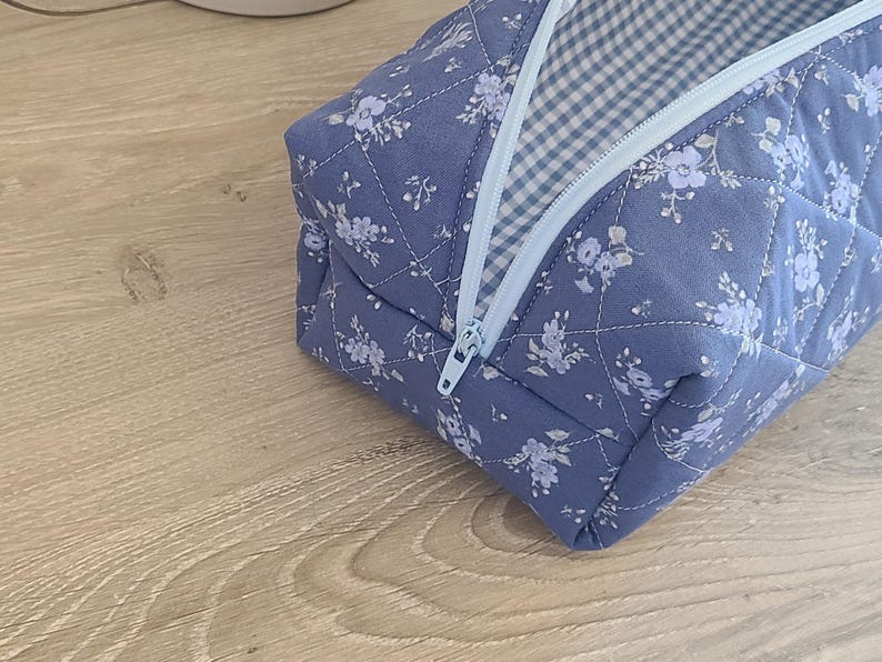 A blue and white floral patterned bag with a zipper closure is placed on a wooden surface.