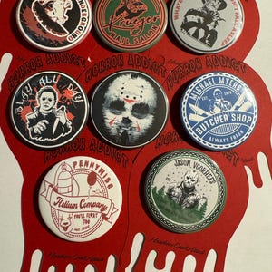 May include: Set of ten 2.25 inch diameter horror movie themed button pins. The pins feature various characters and logos from popular horror movies, including Freddy Krueger, Jason Voorhees, Pennywise, and Michael Myers. The pins are red, white, blue, green, and black.
