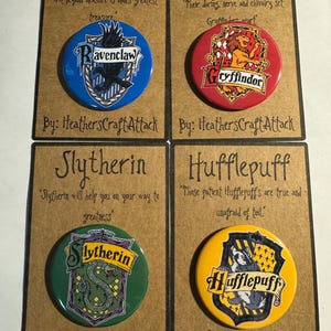 May include: Four round button pins featuring the emblems of Ravenclaw, Gryffindor, Slytherin, and Hufflepuff. Each pin is on a brown card with text. The Ravenclaw pin is blue, the Gryffindor pin is red, the Slytherin pin is green, and the Hufflepuff pin is yellow.