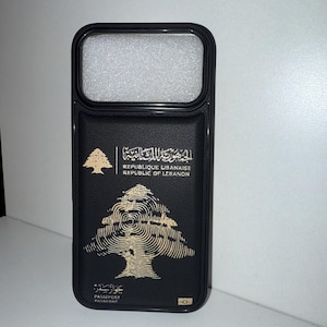 May include: Black phone case featuring the Lebanese passport design. The case has a rectangular camera cutout at the top and a gold emblem of a cedar tree. The text "REPUBLIQUE LIBANAISE REPUBLIC OF LEBANON" is printed above the tree.