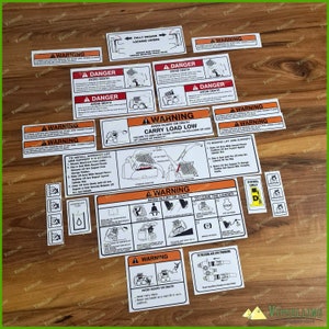 Peut inclure: Un ensemble d'étiquettes d'avertissement et d'instructions blanches et noires avec des accents rouges et orange. Les étiquettes comportent du texte tel que "Danger Avoid Death" et "Warning Avoid Injury or Death". Pour un chargeur ou engin similaire.