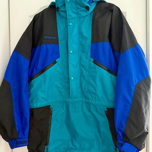 May include: A vintage Columbia anorak jacket in teal, black, and blue. The jacket features a hood, snap closures, and zippered pockets. The Columbia logo is visible on the chest.