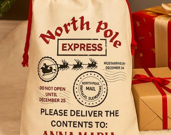 Può includere: Un sacco regalo di Natale color crema con dettagli rossi e testo. La borsa recita "North Pole Express" e include un indirizzo di consegna per "Anna Maria". La borsa è vicino a un albero di Natale e regali confezionati.