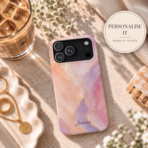 May include: A smartphone case featuring a swirling marble pattern in shades of peach, pink, and lavender with gold veining accents. The name Jessica is printed in gold script at the bottom. A circular label reads PERSONALIZE IT Name or initials.