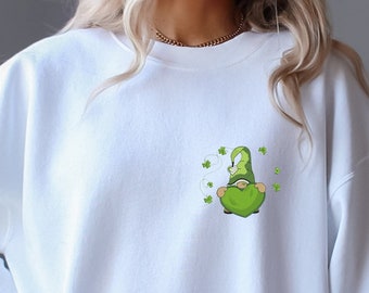 Puede incluir: Sudadera blanca con un diseño de gnomo del Día de San Patricio. El gráfico incluye un gnomo verde con un gorro puntiagudo y tréboles. El diseño está en la parte delantera de la sudadera. La sudadera es de material suave.