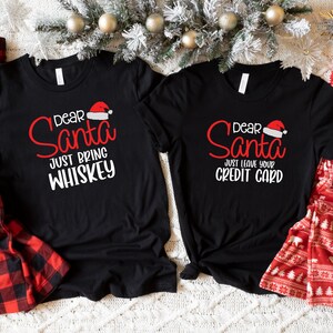 May include: Two black t-shirts with a Christmas theme. The left shirt says "Dear Santa Just Bring Whiskey" and the right shirt says "Dear Santa Just Leave Your Credit Card".