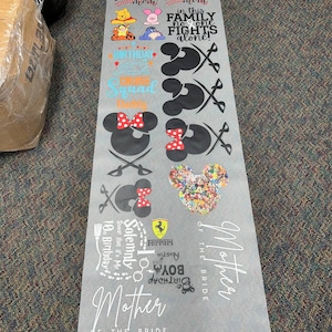 May include: A sheet of white vinyl with black and colored text and images. The text includes "Baseball Mom", "In this family no one fights alone", "Birthday Cruise Squad", "Solemnly swear that it's my 10th birthday", "Ferrari", "Austin Boy Birthday 2023", and "Mother of the Bride". The images include Mickey Mouse, Minnie Mouse, a baseball, a cruise ship, a Ferrari logo, and a birthday cake.