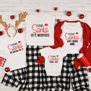 May include: A family of four matching Christmas pajamas with a black and white plaid pattern. The shirts feature the text "Dear Santa" with different messages. The adult shirts say "Let's Negotiate" and "Just Bring Wine". The child's shirt says "My Brother Did It!" and the baby's shirt says "Your Text".