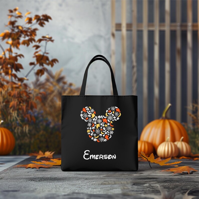 Pode incluir: Sacola de tecido preta para Halloween com um design de cabe&ccedil;a do Mickey Mouse feito de &iacute;cones de Halloween. A sacola tem uma al&ccedil;a branca e o nome "EMERSON" impresso abaixo do design.