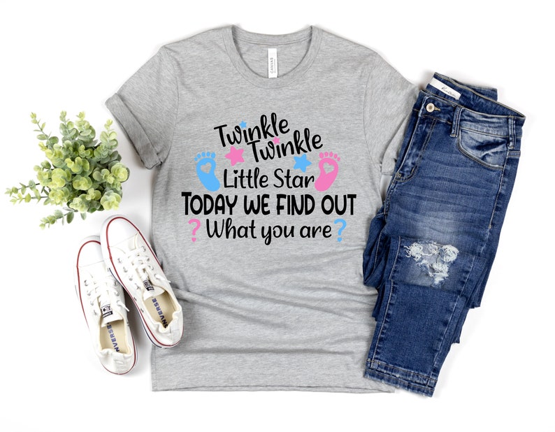 May include: A gray t-shirt with the text "Twinkle Twinkle Little Star Today We Find Out What You Are?" in black. The text is surrounded by two pink and blue footprints and stars.