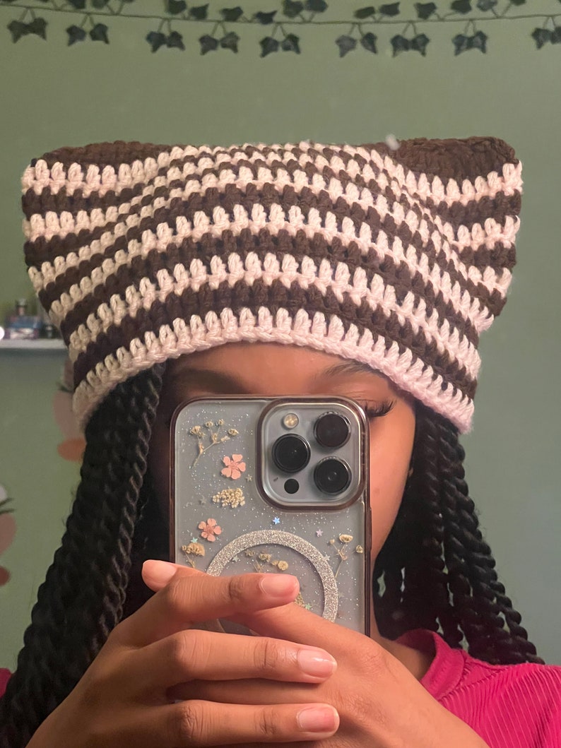 May include: A brown and pink striped crocheted hat with cat ears.