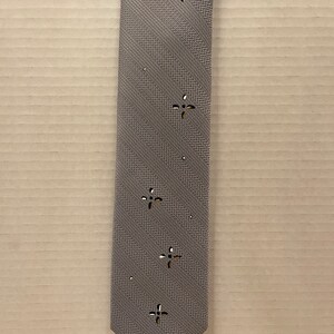 May include: A gray patterned tie with a subtle striped design and a repeating cutout star pattern.