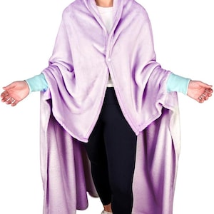 May include: A purple wearable blanket with sleeves. The blanket is made of soft, plush fabric and has a shawl collar. The person wearing the blanket is standing and looking down.