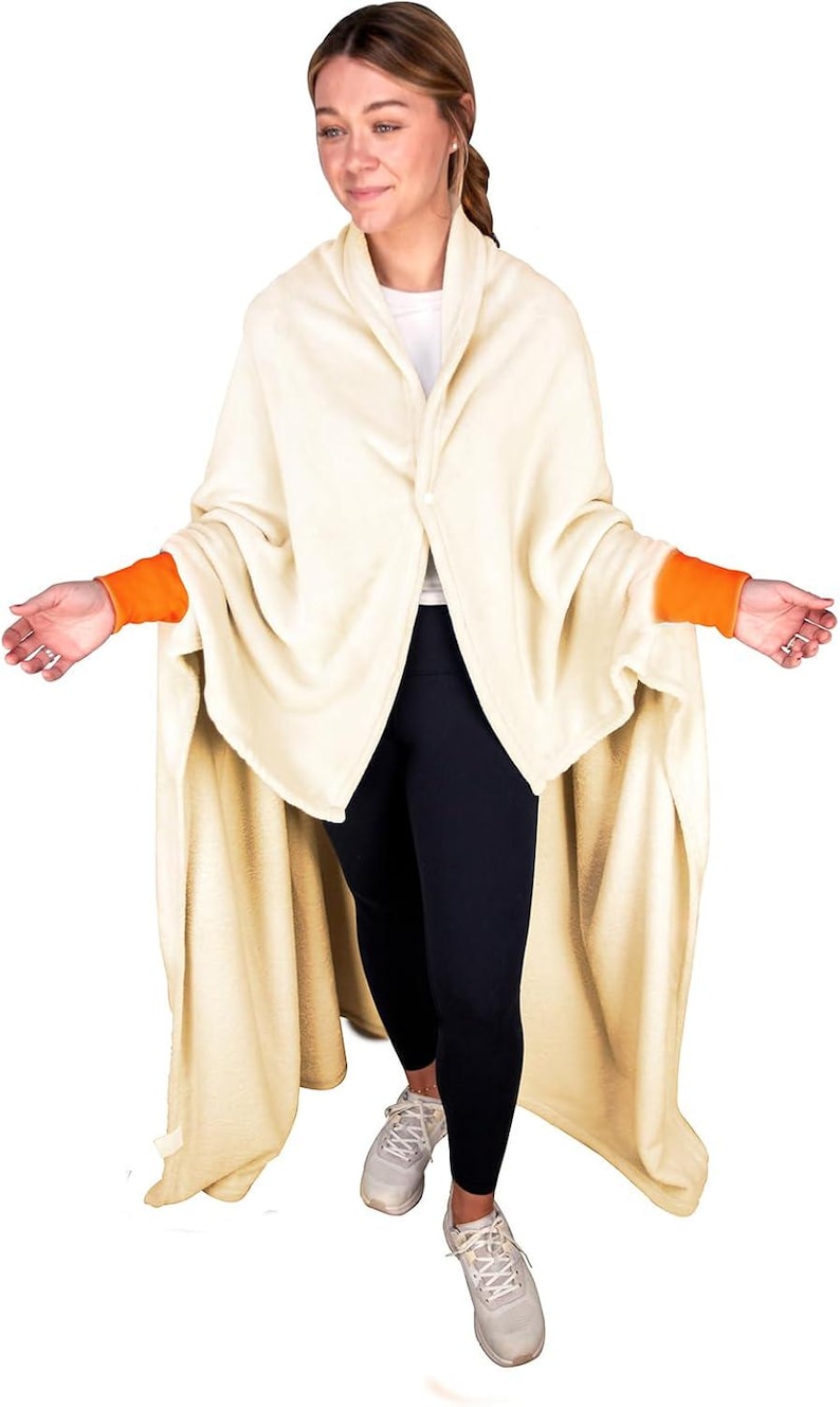 Puede incluir: Una manta de forro polar de color crema con ribetes naranjas en las mangas. La manta se lleva como una bata y tiene un cuello chal.