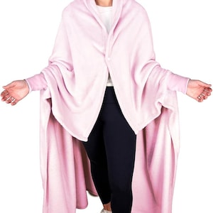 May include: A pink wearable blanket with sleeves. The blanket is made of soft fleece and has a shawl collar. The model is wearing black leggings and white sneakers.
