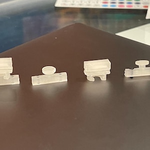 May include: Four clear plastic 3D printed objects. The objects are different sizes and shapes. The objects are on a dark gray surface.