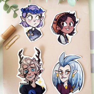 May include: Four character stickers featuring illustrations of characters with unique hairstyles and outfits. One character wears a flower crown, another a beanie, and a third has antlers. Each sticker has a unique design and color palette.