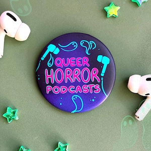 May include: A round button with a dark purple background and a white outline. The button has a pink and blue design with the text "Queer Horror Podcasts" in a white outline.